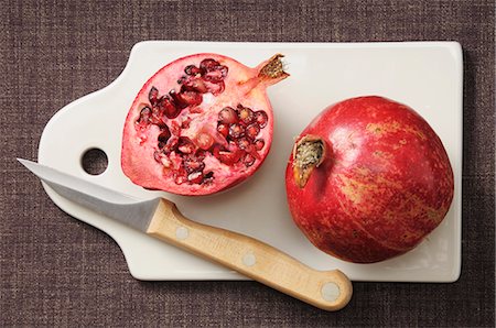 A whole and a half pomegranate on a chopping board with a knife Foto de stock - Sin royalties Premium, Código: 659-07027917