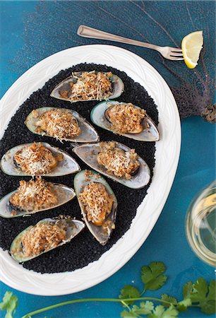 shellfish recipe - Green mussels topped with cheese and grilled, on a white plate with black salt Foto de stock - Sin royalties Premium, Código: 659-07028352