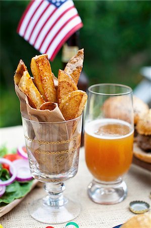 summer beer - Potato wedges on a table outside, in the background buffalo burgers and a US flag Stock Photo - Premium Royalty-Free, Code: 659-07028365