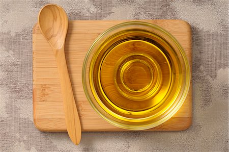 Olive oil in a glass dish on a chopping board with a wooden spoon Photographie de stock - Premium Libres de Droits, Code: 659-07068974