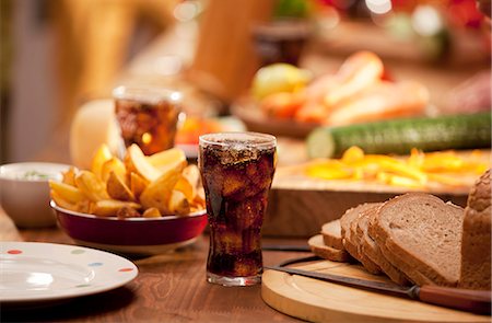 fast food - A table set with bread, potato wedges, raw vegetables and cola Photographie de stock - Premium Libres de Droits, Code: 659-07069700