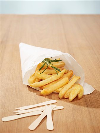 Chips with a sprig of rosemary in a cone of white baking parchment, and wooden chip forks Foto de stock - Royalty Free Premium, Número: 659-07069737