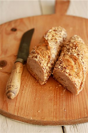 Halved wholegrain baguette with a knife on a wooden board Stock Photo - Premium Royalty-Free, Code: 659-07597138