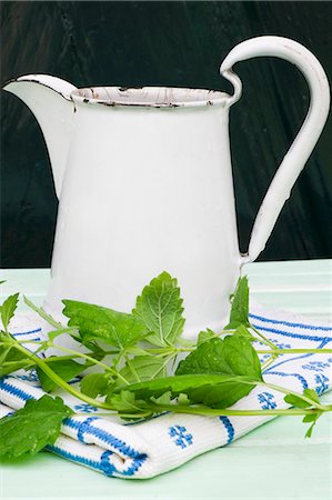 A still life featuring an enamel jug, lemon balm and an embroidered cloth Foto de stock - Sin royalties Premium, Código: 659-07597499