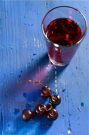 simsearch:659-08420354,k - Cherries and cherry juice on a blue wooden tabletop Photographie de stock - Premium Libres de Droits, Code: 659-07598510