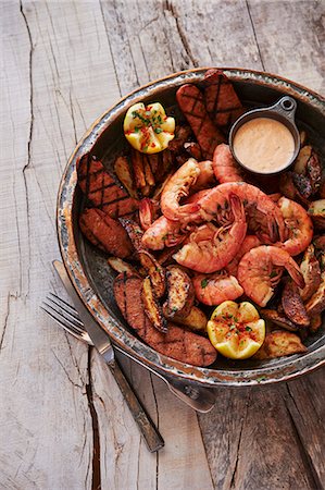 simsearch:659-01867168,k - Shrimp Boil with grilled andouille sausage, fried potatoes, and remoulade sauce on wooden surface Foto de stock - Sin royalties Premium, Código: 659-07609595