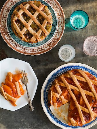 Gooseberry and peach pies with lattuce crust on vintage plates with colored glasses on an antiqued metal surface Photographie de stock - Premium Libres de Droits, Code: 659-07610012