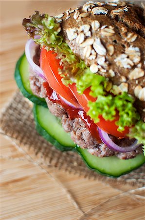 A wholemeal roll with minced beef, kethcup, gherkins, red onions, tomatoes and lollo rosso lettuce Stock Photo - Premium Royalty-Free, Code: 659-07610207