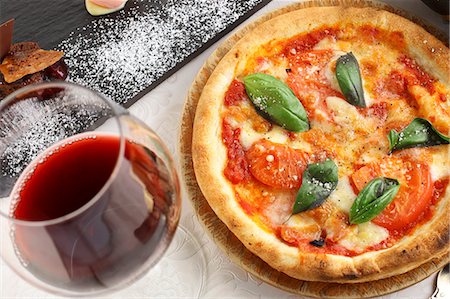 Pizza Napoli with tomatoes, cheese and basil served with a glass of red wine Stock Photo - Premium Royalty-Free, Code: 659-07959564