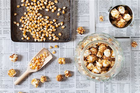 A jar of caramel popcorn next to kernels on a baking tray Stock Photo - Premium Royalty-Free, Code: 659-07959768