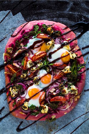 Beetroot pizza dough with broccolini, red onions, tomatoes, goat's cheese, rocket, cheese, fired eggs and balsamic cream Stock Photo - Premium Royalty-Free, Code: 659-07959950