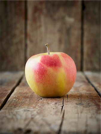 A red and yellow apple on an old, brown wooden surface in front of a wooden wall Stock Photo - Premium Royalty-Free, Code: 659-08147416