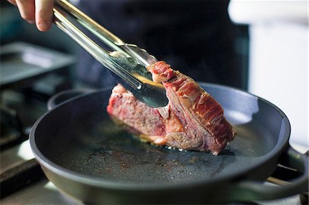 sauteeing - A chef preparing a steak in a commercial kitchen Photographie de stock - Premium Libres de Droits, Code: 659-08147606