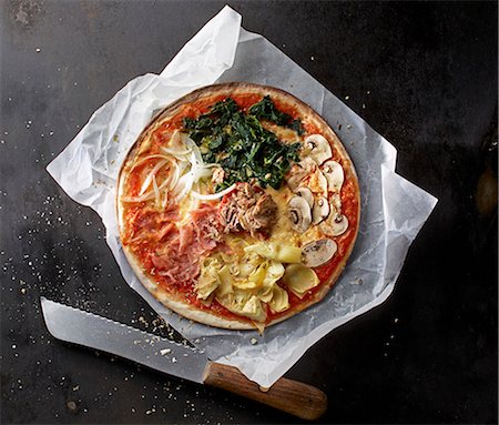 simsearch:659-06154096,k - A pizza with spinach, mushrooms, artichokes, Parma ham, onions and tuna fish on a piece of paper with a knife Stock Photo - Premium Royalty-Free, Code: 659-08147616