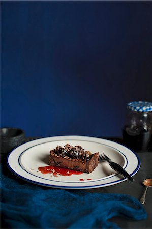 A slice of dark chocolate and cherry tart on a white plate with a blue rim and fork Stock Photo - Premium Royalty-Free, Code: 659-08148169