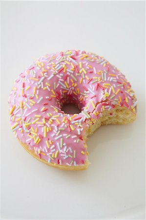 pink donut studio shot - A pink iced doughnut with sugar sprinkles and a bite taken out Stock Photo - Premium Royalty-Free, Code: 659-08148172