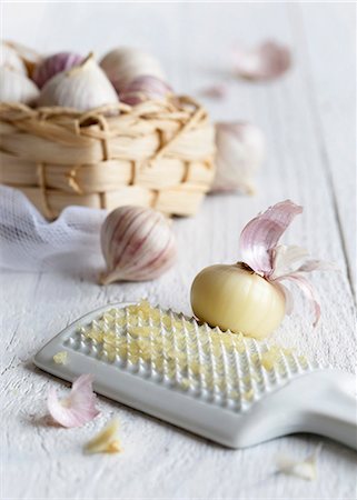 simsearch:659-06495161,k - Peeled single clove garlic grated on a white ceramic grater with a straw basket full of unpeeled single clove garlics Stock Photo - Premium Royalty-Free, Code: 659-08897125