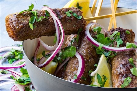 Cevapcici on wooden skewers with onions, parsley and lemon in a grey bowl Stock Photo - Premium Royalty-Free, Code: 659-08904737