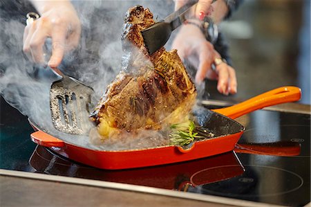 A T-bone steak with rosemary being turned in a pan Stock Photo - Premium Royalty-Free, Code: 659-08905008