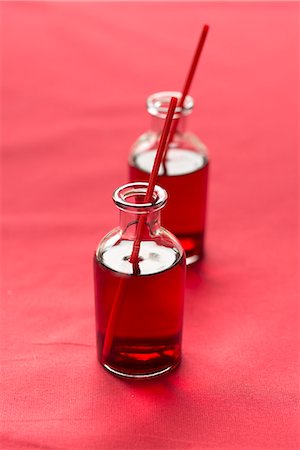 Cranberry juice with straws in small glass bottles on a red surface Stock Photo - Premium Royalty-Free, Code: 659-08906297