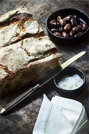 farmhouse bread - An arrangement of crusty bread, olives, sea salt, a knife and a fabric napkin Foto de stock - Sin royalties Premium, Código: 659-08906356