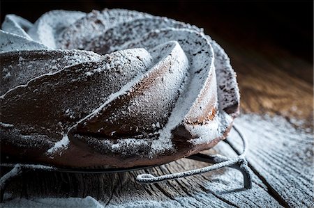 Dark chocolate cake dusted with icing sugar on a wooden table Stock Photo - Premium Royalty-Free, Code: 659-08906506