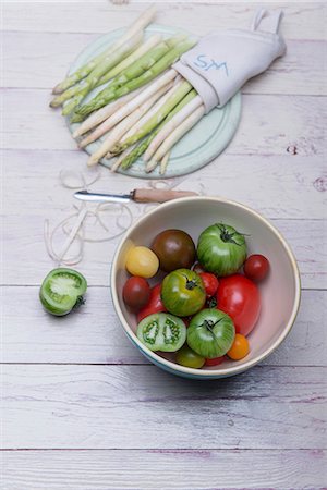 White and green asparagus on a wooden board, asparagus peelings, a peeler and a bowl of various tomatoes Foto de stock - Sin royalties Premium, Código: 659-08903472