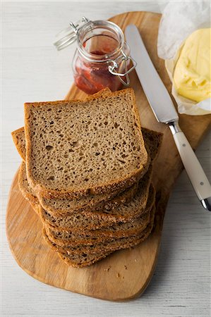 simsearch:659-06151745,k - Slices of wholemeal bread stacked on a wooden board with butter and strawberry jam Stock Photo - Premium Royalty-Free, Code: 659-08903651