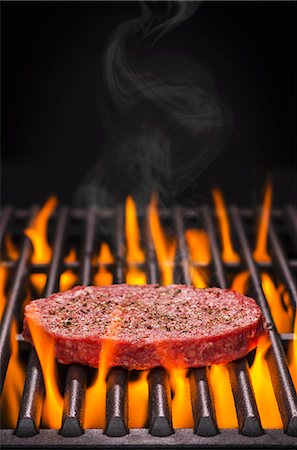 A raw hamburger with salt and pepper on a flaming barbecue Stock Photo - Premium Royalty-Free, Code: 659-08939895