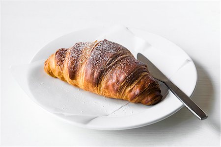 A croissant on a white plate with a knife Stock Photo - Premium Royalty-Free, Code: 659-08940810