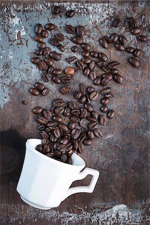 symbolic picture - Coffee beans scattered over a rustic surface with a white coffee cup Stock Photo - Premium Royalty-Free, Code: 659-08941010