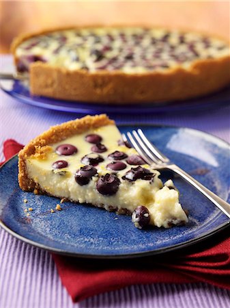 A slice of blueberry lemon pie on a plate with a whole pie in the background Stock Photo - Premium Royalty-Free, Code: 659-09124510