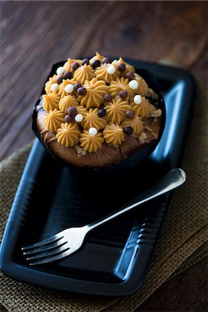 A salted caramel cupcake on a black plate with a fork Stock Photo - Premium Royalty-Free, Code: 659-09125403