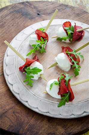 Buffalo mozzarella bites with bresaola and fresh rocket leaves canapes on a white wooden board and wooden background Stock Photo - Premium Royalty-Free, Code: 659-09125758