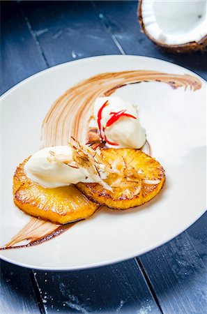 sorbetto - Honey glazed grilled pinapple with coconut sorbet ice cream, essiccated coconut flakes and chilli on a white plate and blue table Stock Photo - Premium Royalty-Free, Code: 659-09125766