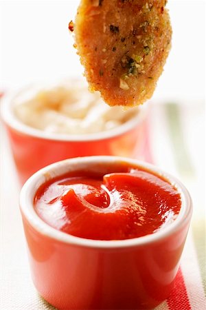 Dipping chicken nugget into ketchup Stock Photo - Premium Royalty-Free, Code: 659-01844508