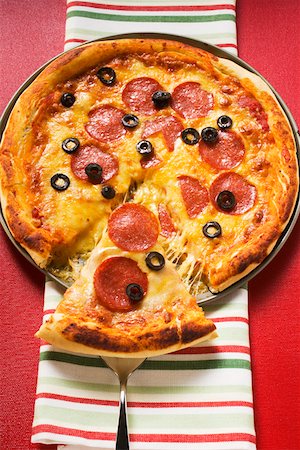 Pizza with salami, cheese and olives, a piece cut Fotografie stock - Premium Royalty-Free, Codice: 659-01846470