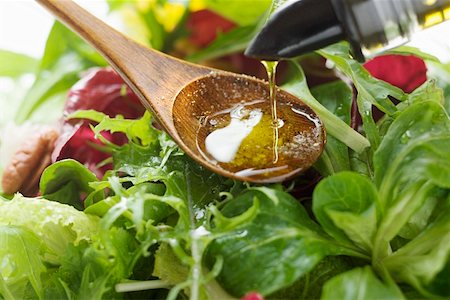 Pouring olive oil into wooden spoon above salad leaves Fotografie stock - Premium Royalty-Free, Codice: 659-01847398