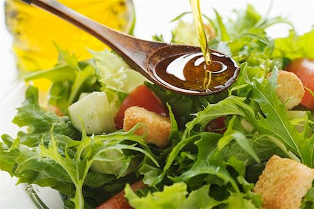 Pouring olive oil into wooden spoon above salad leaves Fotografie stock - Premium Royalty-Free, Codice: 659-01847407