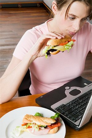 Jeune femme mangeant un sandwich alors qu'il travaillait à l'ordinateur Photographie de stock - Premium Libres de Droits, Code: 659-01847488