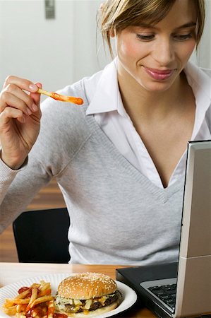 Woman eating hamburger & chips while working at computer Stock Photo - Premium Royalty-Free, Code: 659-01847492