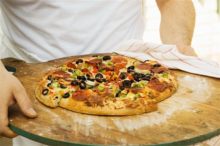 Person holding pepperoni pizza with peppers and olives Stock Photo - Premium Royalty-Free, Code: 659-01847557