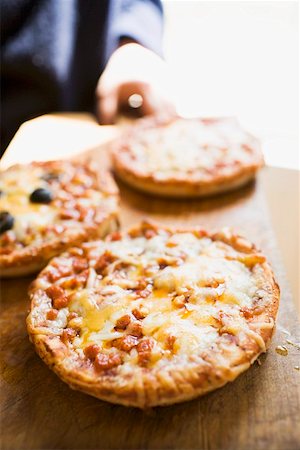 Person holding wooden board with three mini-pizzas Stock Photo - Premium Royalty-Free, Code: 659-01847704