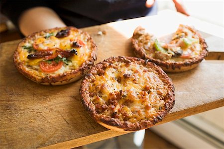 Person holding wooden board with three different mini-pizzas Stock Photo - Premium Royalty-Free, Code: 659-01847701