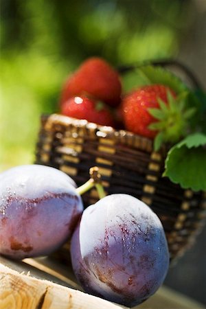 fruit still life - Two plums with drops of water, strawberries in basket behind Stock Photo - Premium Royalty-Free, Code: 659-01857704