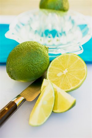 Limes, whole, halved and wedges, squeezer in background Stock Photo - Premium Royalty-Free, Code: 659-01864133