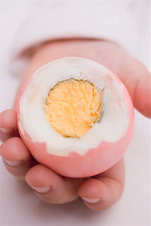 Child's hands holding coloured boiled egg with top cut off Stock Photo - Premium Royalty-Free, Code: 659-01864325