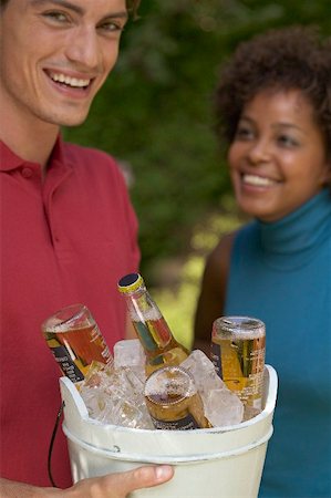 Man holding ice bucket full of beer bottles, woman in background Stock Photo - Premium Royalty-Free, Code: 659-01867644