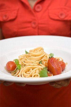 Woman holding plate of spaghetti with tomatoes and basil Stock Photo - Premium Royalty-Free, Code: 659-01860522