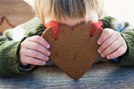 Small boy holding gingerbread heart in front of his face Foto de stock - Royalty Free Premium, Número: 659-01861810
